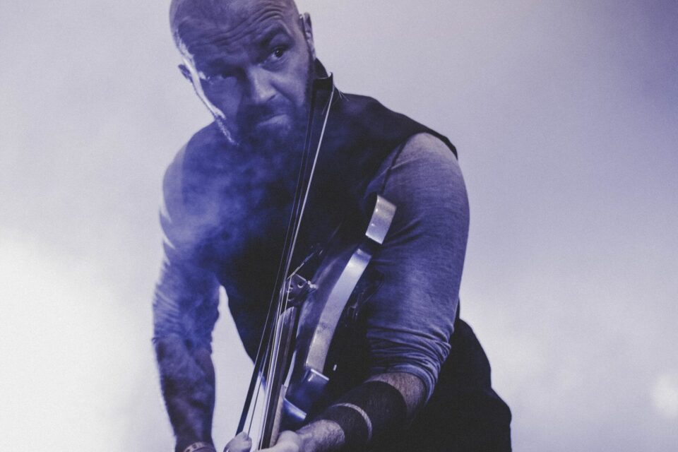 Nærbilde av mann, overkropp og hode, som spiller fele på scene i lilla lys