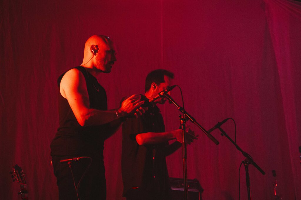 To musikere klapper foran hver sin mikrofon, i rødt scenelys.